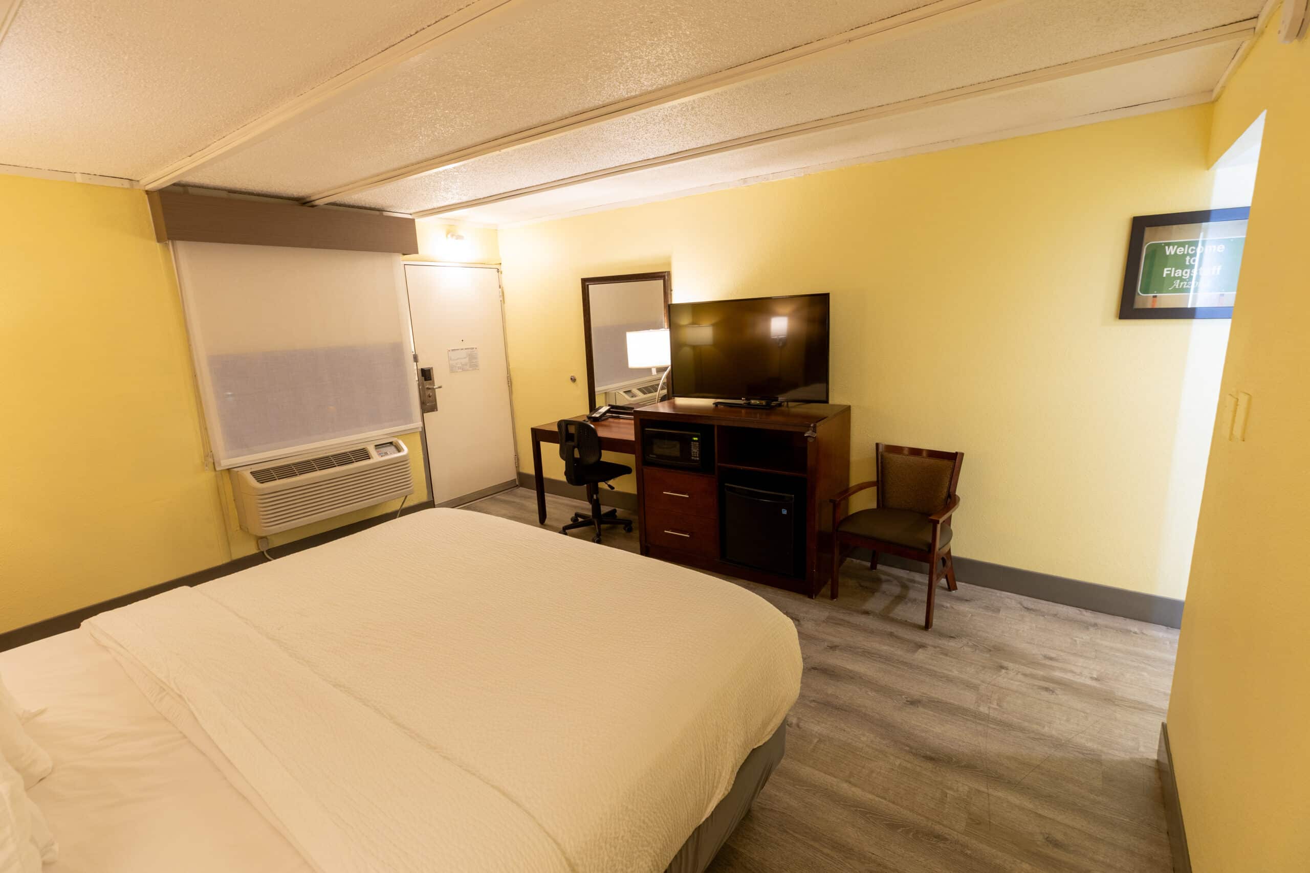 Kings House king room with bed in foreground, TV console, desk area, and seating chair