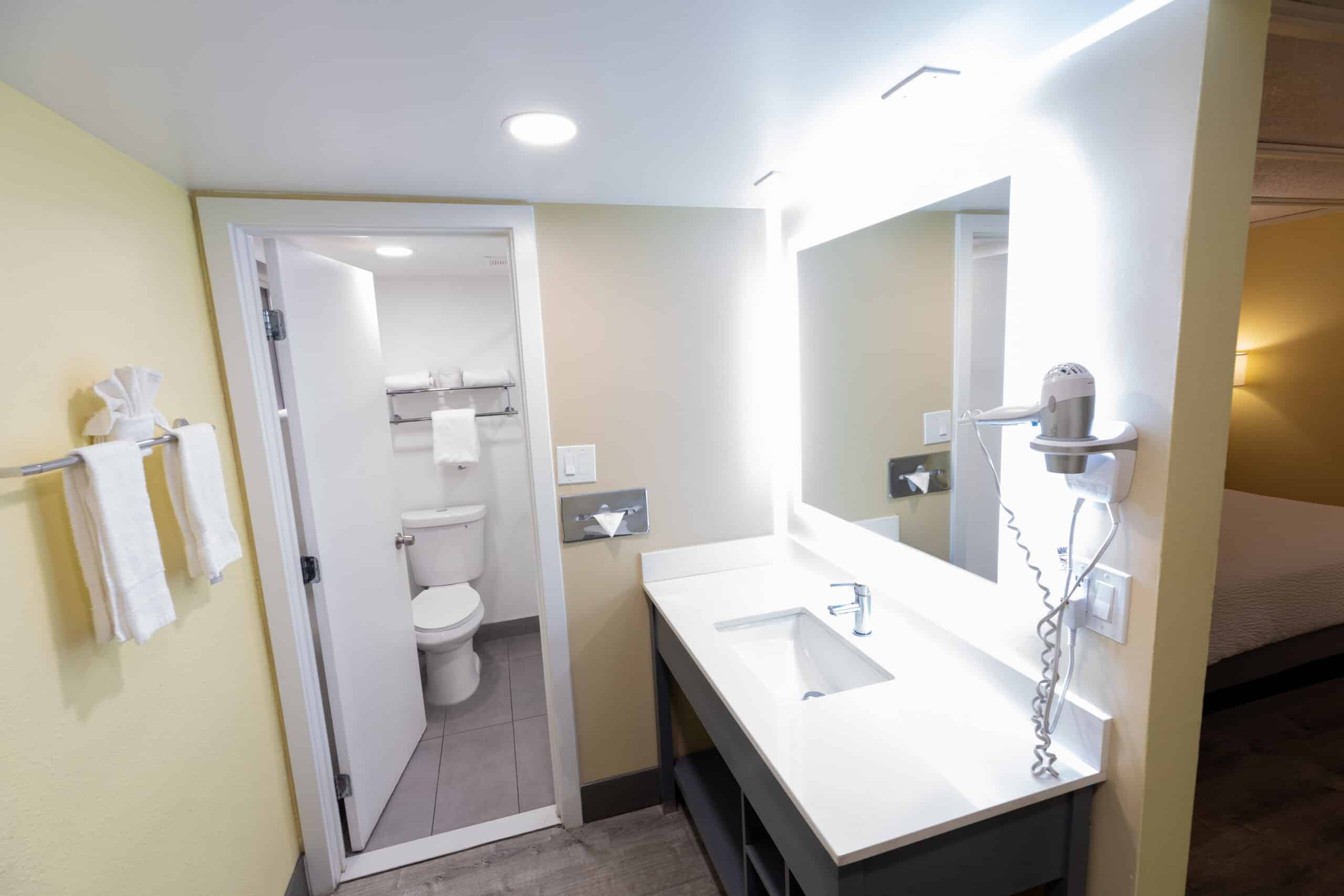 Kings House vanity with lighted mirror, sink, towels, and bathroom doorway