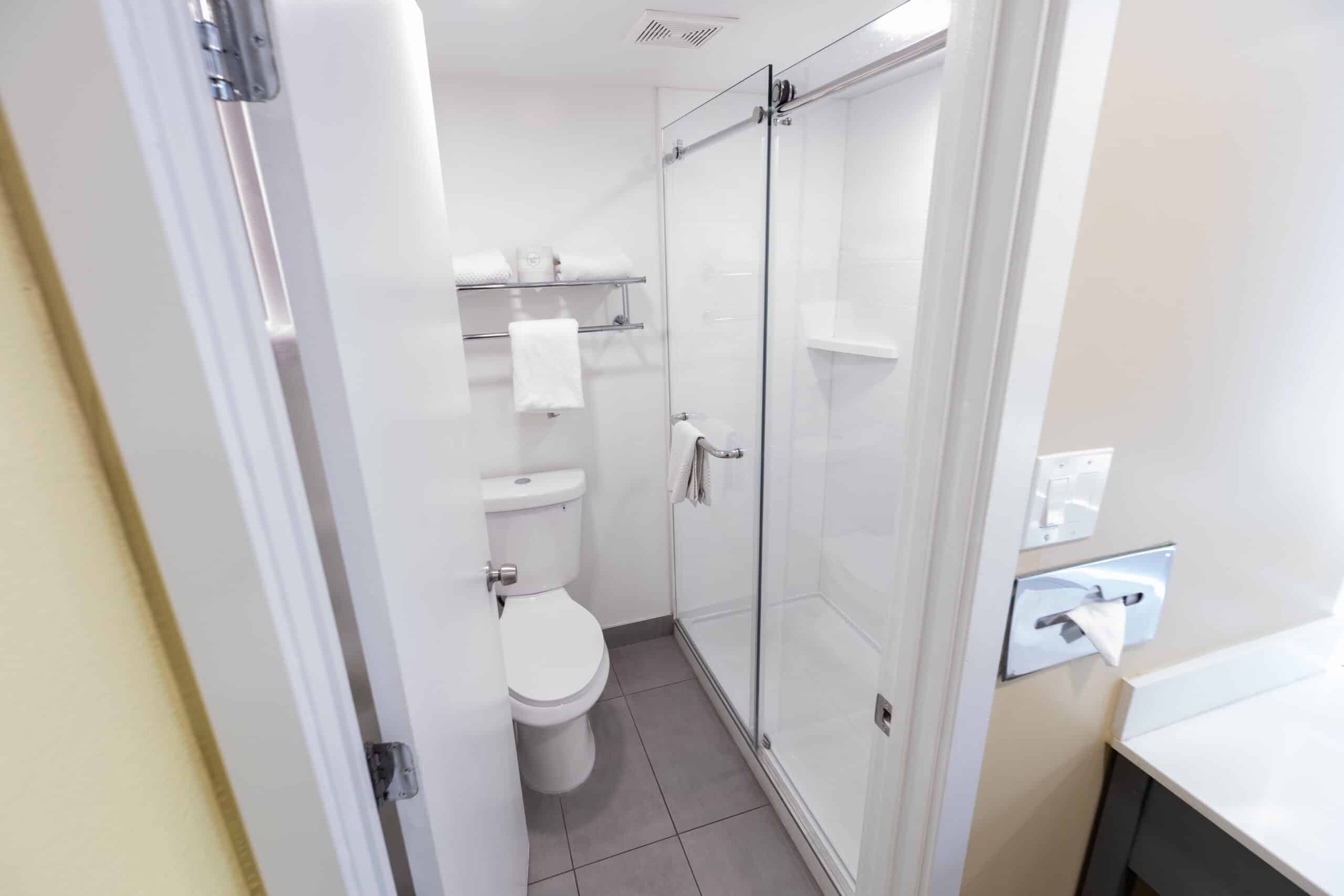 Kings House bathroom with glass shower, toilet, towel shelves, and tiled floor
