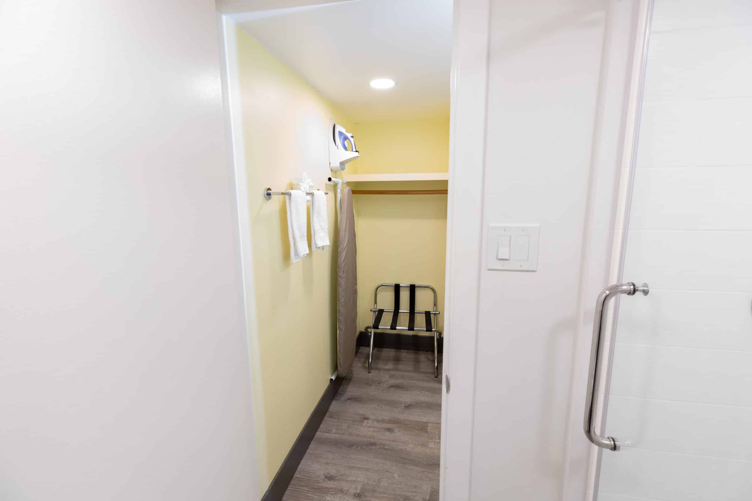 View into closet nook from bathroom with luggage rack, towel bar, and ironing board beside shower door.