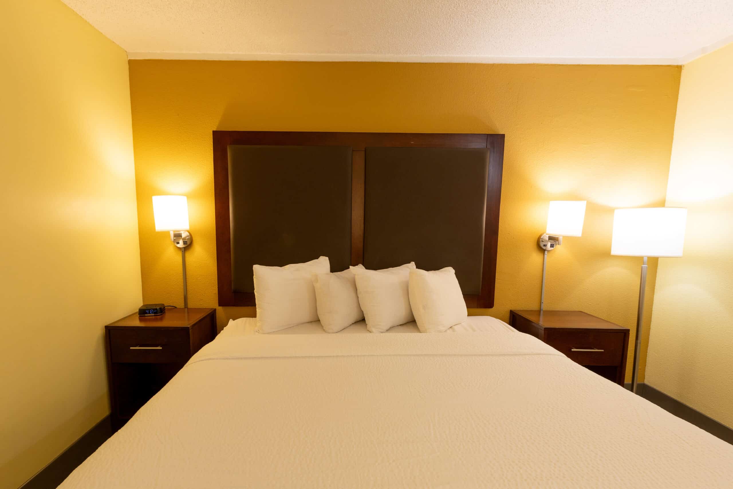 Straight-on view of a king bed with dark headboard, bedside lamps, matching nightstands, and warm accent wall lighting.