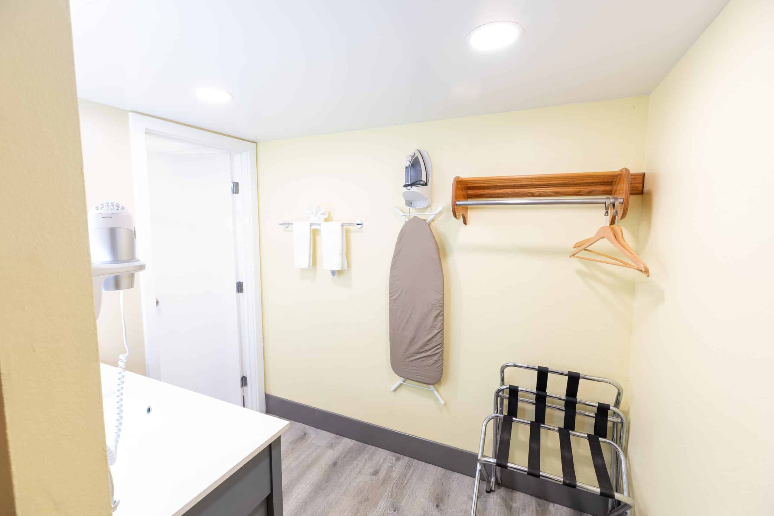 Vanity and closet area with hangers, luggage rack, ironing board, towels, and hair dryer at Kings House