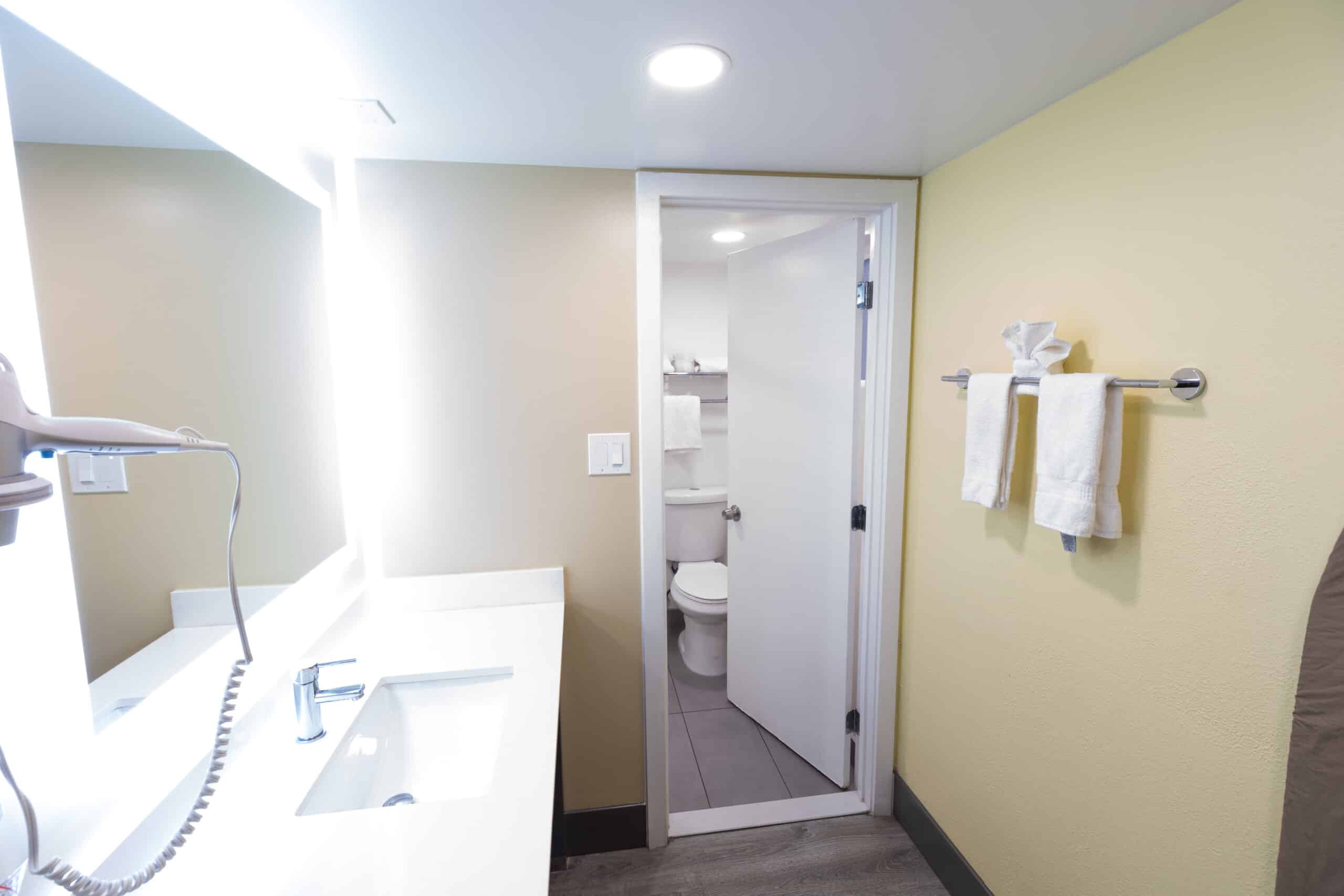 Bright vanity sink with lighted mirror and towels, leading into bathroom at Kings House