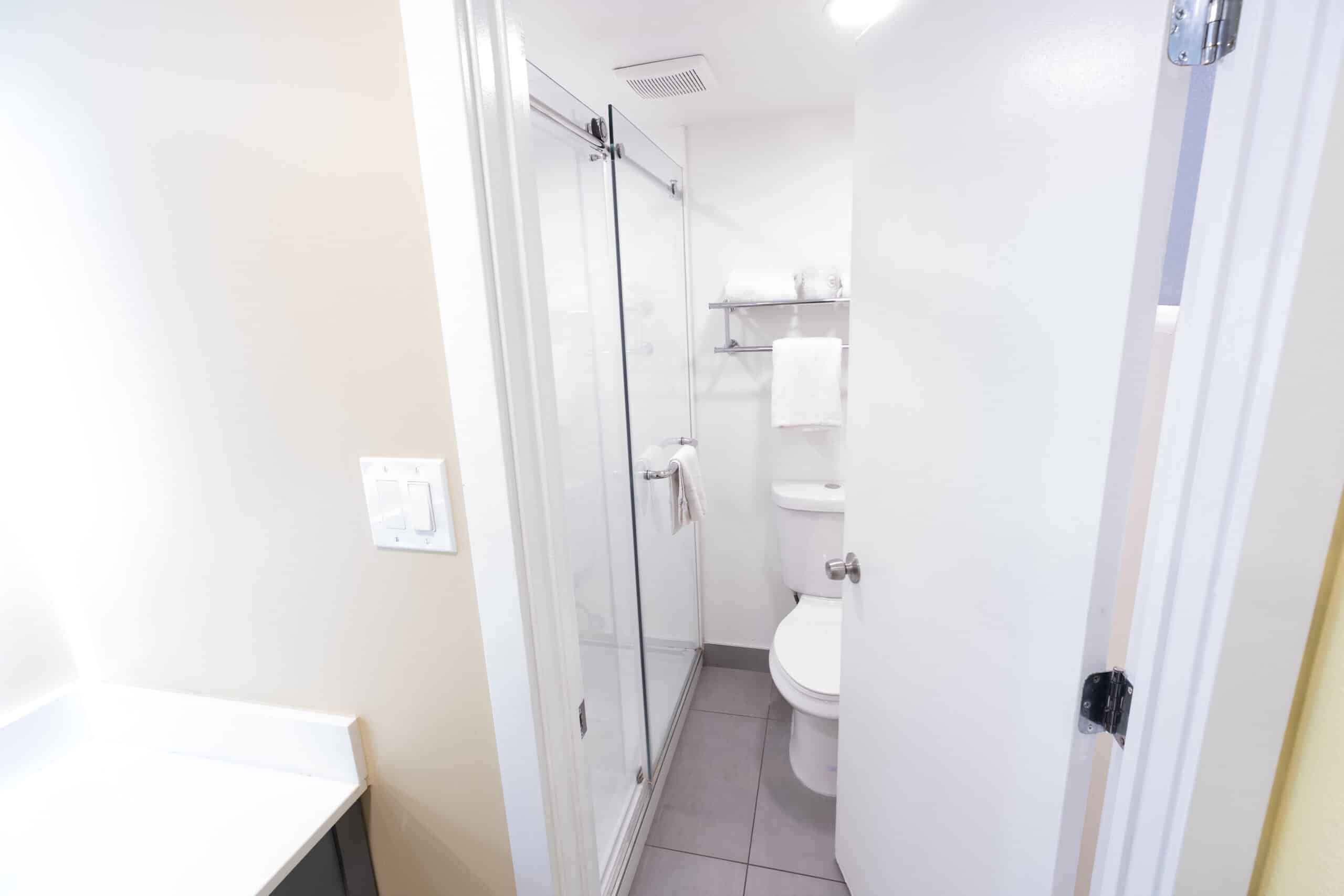 Updated bathroom with glass shower, toilet, and towel shelving in Kings House guest room