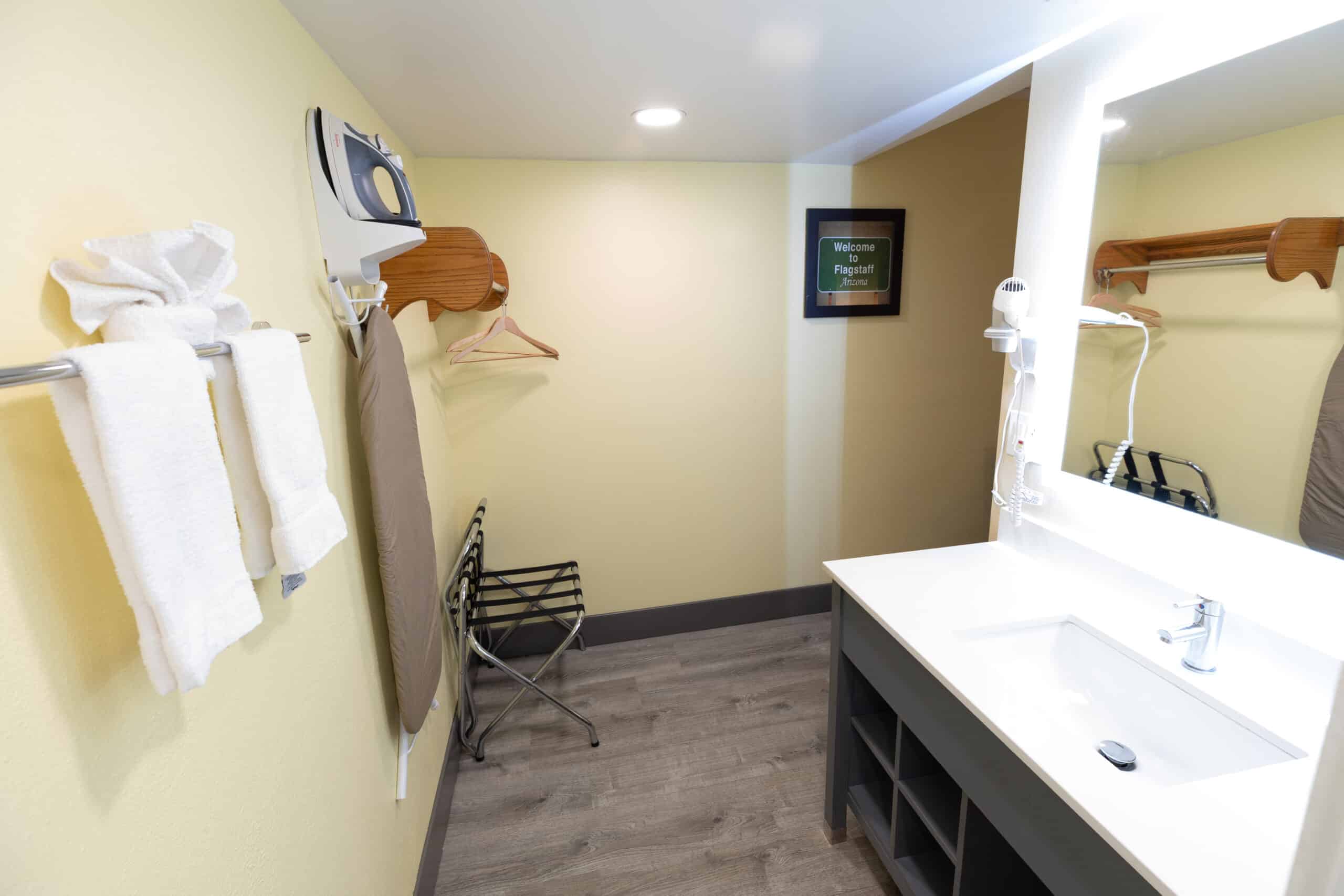 Spacious vanity area with large sink counter, lit mirror, hangers, ironing board, and luggage rack