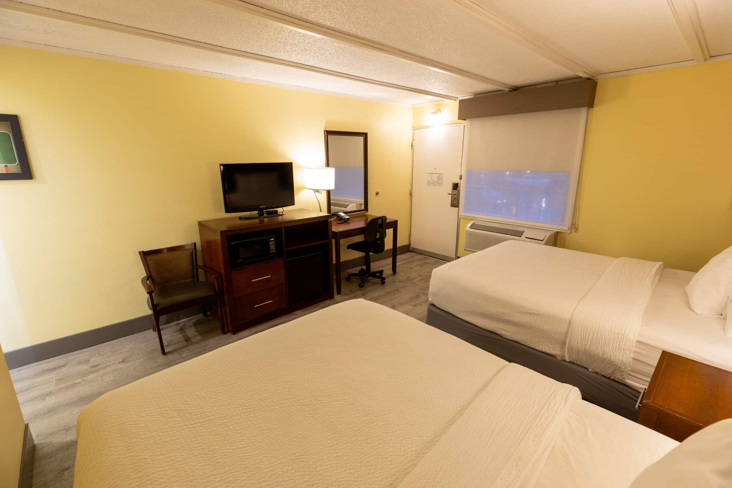 Two queen room with TV console, microwave, mini fridge, desk, chair, and window A/C at Kings House